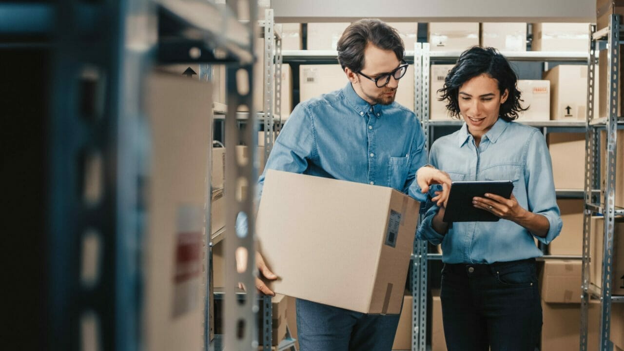 Female Inventory Manager Sharing Digital Information With Male Employee Via Tablet In A Warehouse Setting.