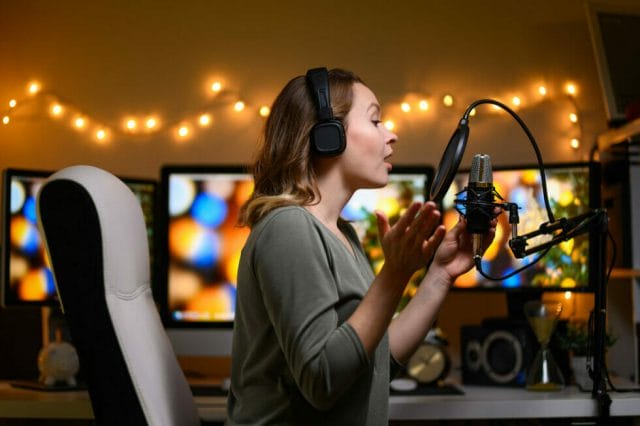 Influencer recording video commentary with studio microphone at a desk. multi-monitor workstation