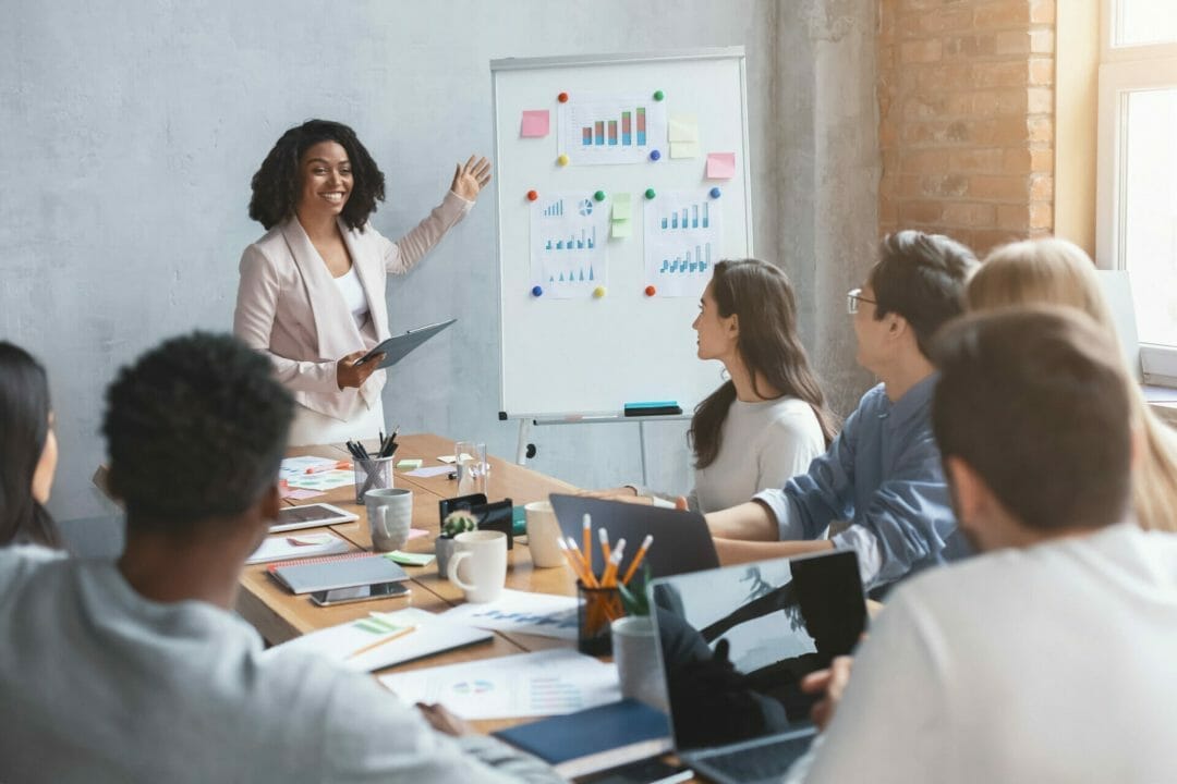 Female Marketing Professional Presenting New Lead Data On A Whiteboard To Business Team.